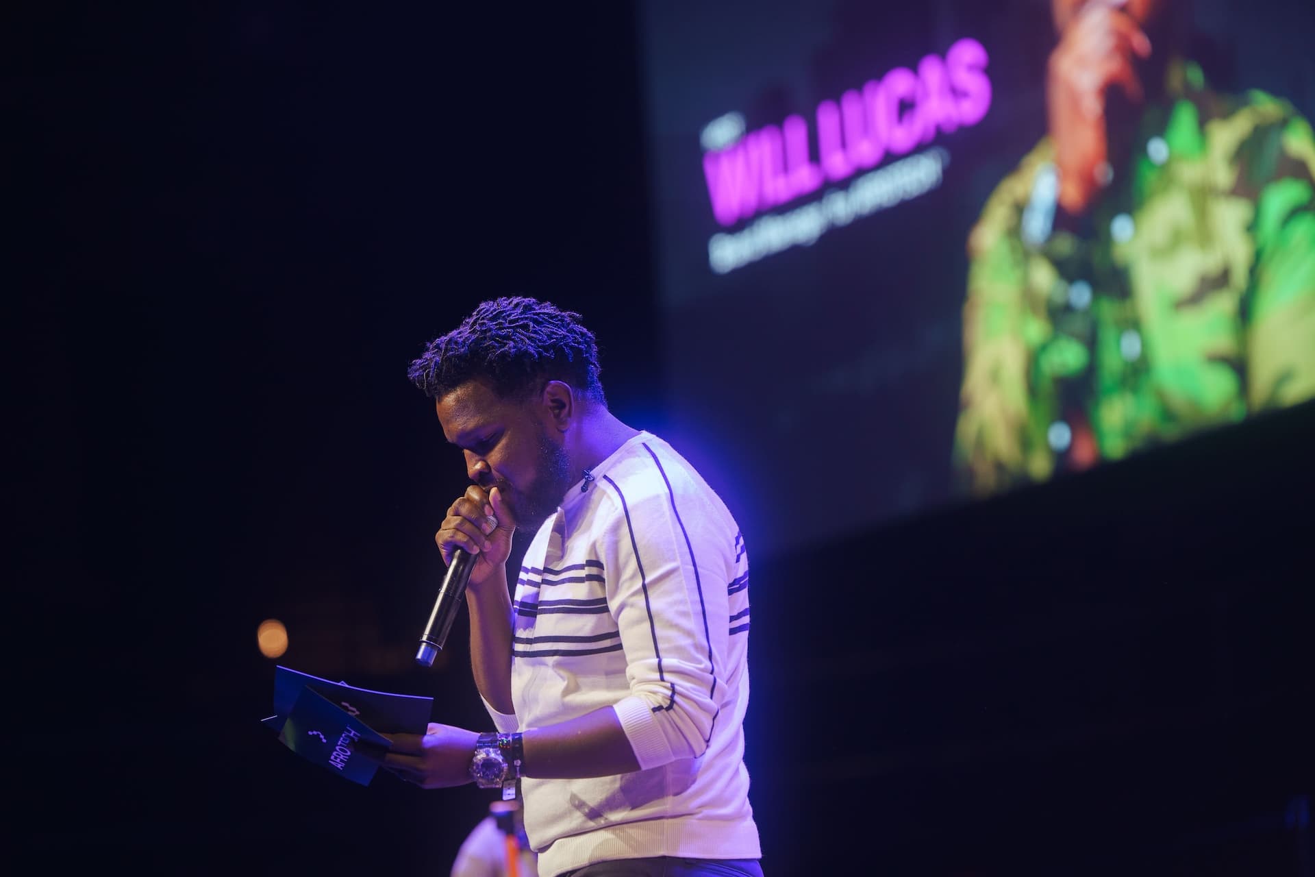 Will Lucas speaking from a podium with "WILL LUCAS" projected on the screen behind him.